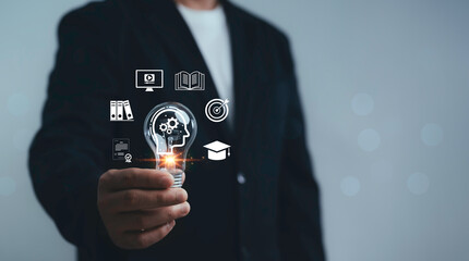 Businessman holding light bulb with human head gear and education icons representing learning knowledge innovation skill development and training concept in professional business growth