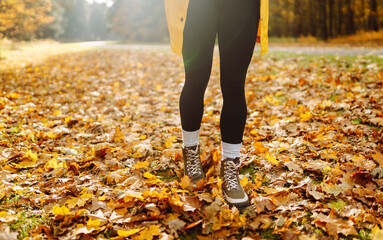 A close-up of a hiker's legs in hiking boots standing on a walking trail surrounded by colorful autumn leaves. A woman in raincoat and boots enjoys autumn day in park. Adventure concept.