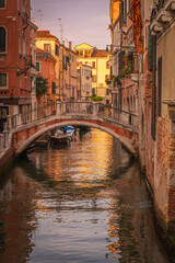 Venetian canal with stone pedestrian bridge at sunset