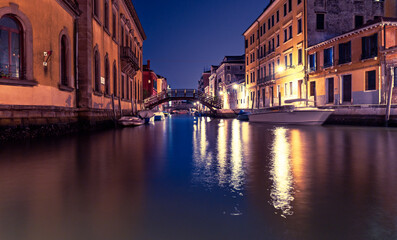 Quiet Venetian canal with illuminated bridge at night