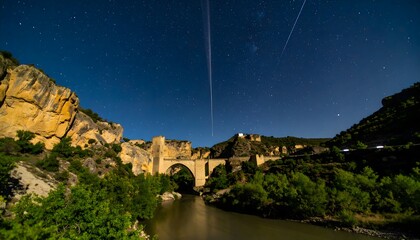 Old stone bridge and riverfront at night with a Perseid—historic arches and city lights beneath a...