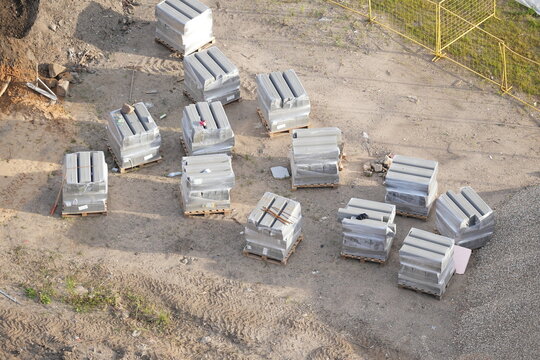 Stacks of concrete curbs wrapped in plastic and placed on wooden pallets at a construction site. Building materials prepared for road construction and urban infrastructure projects.
