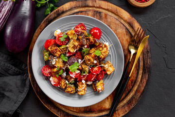  Georgian salad with deep fried eggplant, tomatoes, onions, feta cheese and cilantro on the black background. Vegetarian food with eggplant and other vegetables, top view