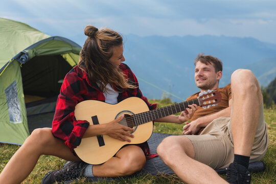 Young couple camping in the mountains, playing guitar, enjoying freedom and connecting with stunning nature. - Powered by Adobe