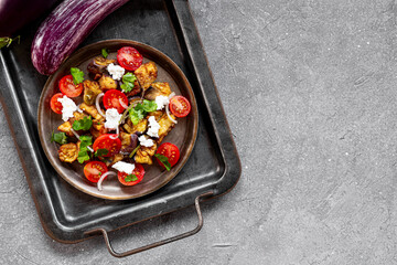  Georgian salad with deep fried eggplant, tomatoes, onions, feta cheese and cilantro on the grey backgraund. Vegetarian food with eggplant and other vegetables, top view