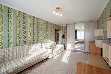 Cozy living room with sofas, patterned wallpaper, and a large wardrobe with mirrored doors....