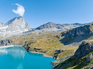 Aerial view of the Matterhorn, seen from Breuil-Cervinia. Green valleys and waterways flowing from the glaciers. Goillet reservoir and dam. Italy