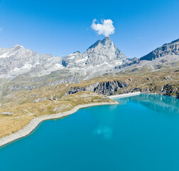 Aerial view of the Matterhorn, seen from Breuil-Cervinia. Green valleys and waterways flowing from the glaciers. Goillet reservoir and dam. Italy