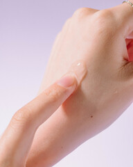 Close-up of a hand applying transparent gel skincare product on the skin, isolated on a pastel background. Beauty and self-care concept showcasing moisturizing gel texture, suitable for cosmetic.