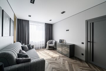 modern living room with gray tones, featuring a sofa, chair, dresser, and herringbone floors. Light...
