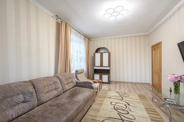 Cozy living room: striped walls, soft sofa, patterned carpet.  Light fixture on the ceiling, glass table with flowers