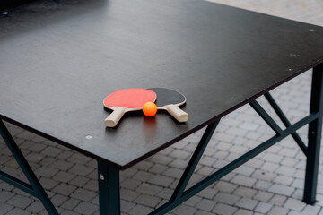 Table tennis paddles and orange ball on a playing table.