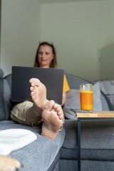 Smiling woman working remotely on laptop while relaxing on the couch at home. Freelance lifestyle,...