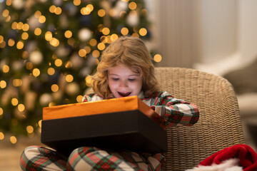 Merry Christmas. Cheerful cute kid boy opening gifts. Kids near tree in the morning. Christmas presents in room. Surprise child opening Christmas magic presents.