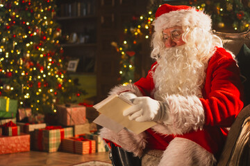 Merry Christmas. Happy Santa Claus reading letters from children in festive Christmas living room....