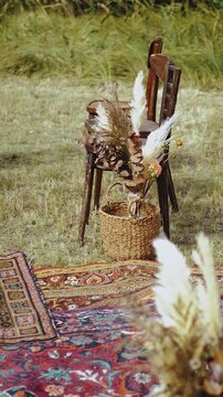 Vertical video. Boho wedding ceremony in the sky. Wooden chairs and embroidered carpet, floral arrangements made of dried flowers. Summer wedding, slow motion. Wedding decor.
