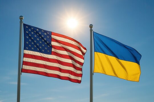United States and Ukraine flags flying side by side against a clear blue sky with the sun shining brightly