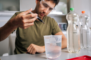 Chemist carefully adding red liquid fertilizer to water in beaker using syringe, preparing solution...