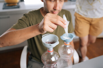 Cropped shot of urban farmer pouring fertilizer components into plastic bottles through funnels, preparing nutrient solution for plants, demonstrating precise approach to plant care.