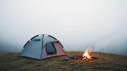 Camping Tent Beside Campfire in Foggy Mountain Meadow