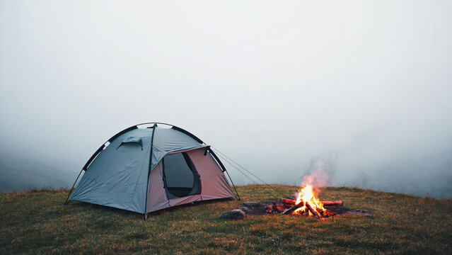 Camping Tent Beside Campfire in Foggy Mountain Meadow - Powered by Adobe