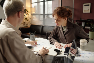 Over shoulder shot of two young male and female business people discussing results of research