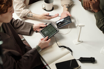 High angle view of unrecognizable coworkers holding portable solar panels discussing renewable...