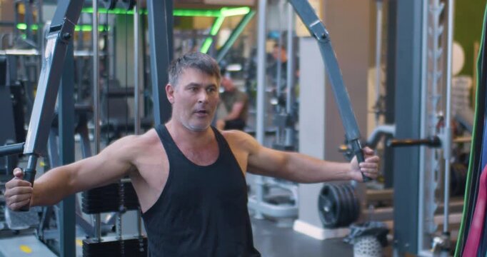 Gym workout. Butterfly exercise. Middle aged Caucasian man trains his pectoral muscles in the gym. Middle-aged man works out chest muscles with butterfly machine at the gym.