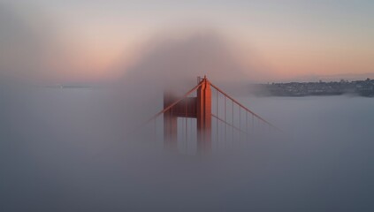 Golden gate bridge partially obscured by fog at sunset with soft pastel sky in the background