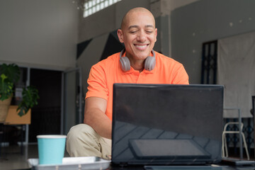 Bald Hispanic man smiling and using laptop computer in coffee shop restaurant