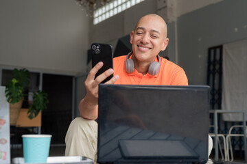 Bald Hispanic man sitting and using laptop computer and phone in coffee shop restaurant