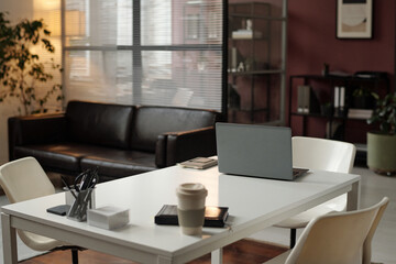 Interior of office with modern design, white desk, ergonomic chairs, laptop, plants and glass wall