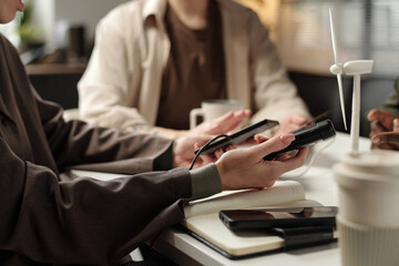 Medium closeup of unrecognizable engineers holding portable gadgets discussing renewable energy...