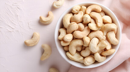 Bowl full of cashew nuts on a textured surface with a delicate pink fabric, showcasing healthy snack.