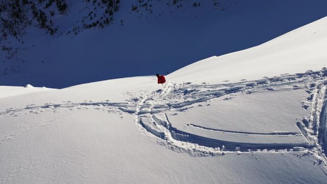 Snowboarder leaving s-shaped trail on snowy mountain slope