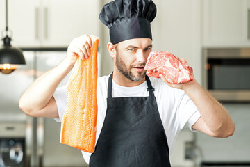 Handsome man cooking fish and meat, salmon and beef in kitchen. Portrait of casual man cooking in...