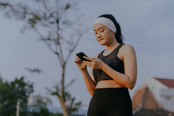 Happy athlete asian woman typing with phone research of exercise application, fitness outdoor and communication, looking training schedule and workout routine. Copy space for text.