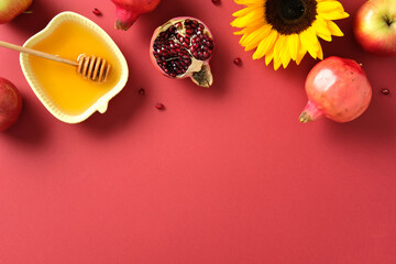 Rosh Hashana, Jewish holiday concept. Flat lay composition with honey, apples, pomegranates, and sunflower on red background.