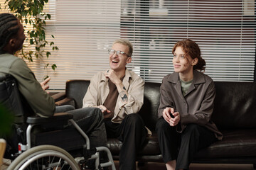 Black man with disability and his Caucasian male and female colleagues having fun chatting during...
