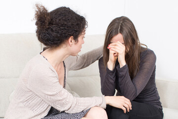 A young woman consoles her crying friend on the sofa, symbolizing therapy, emotional health, crisis...