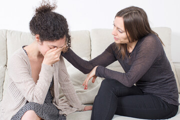 A woman gently consoling her crying friend on the sofa, showing empathy and care.