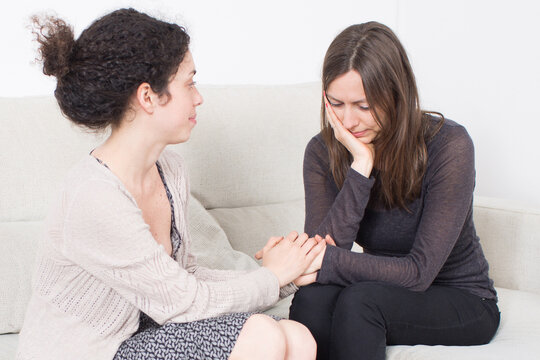 Two women sit together, one holding the other&rsquo;s hands to provide comfort and reassurance. The image reflects empathy, compassion, emotional support, and friendship during sadness.