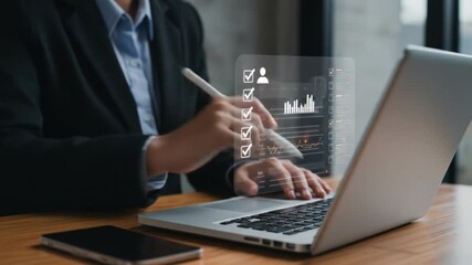 A person in a suit interacts with a digital interface on a laptop with a phone on the table near by - Powered by Adobe