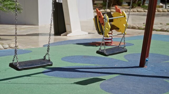 Outdoor playground with swings on sunny day featuring vibrant rubber flooring and children's spring rider creating a cheerful leisure setting.
