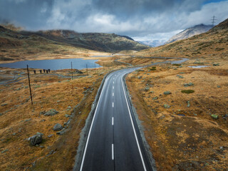 Aerial drone view of wet winding road in the Swiss Alps, Switzerland, with alpine lake, dramatic...