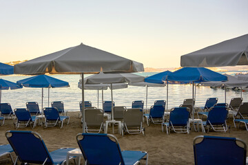 Empty sunbeds with umbrellas on sandy beach by the sea. Relaxing summer holiday atmosphere at...