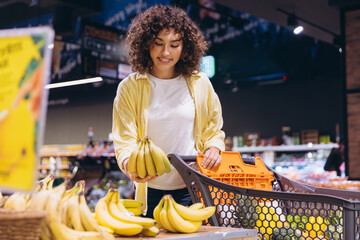 Woman choosing bananas in supermarket with shopping cart