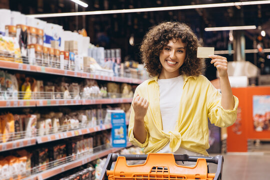 Woman pushing shopping cart and showing fidelity card in supermarket