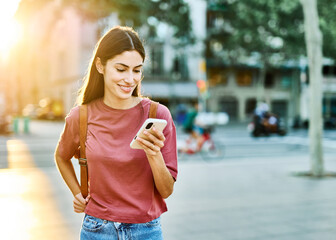 Young woman enjoys sunny day while using smartphone in urban setting, highlighting her joy and...