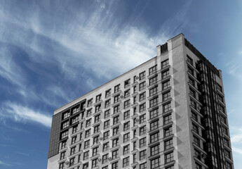 Fototapeta premium Building rises under cloudy sky. Modern concrete multistorey facade overlooks metropolitan